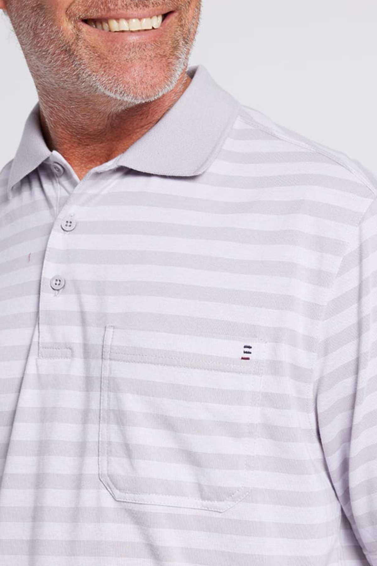 A close-up image of a smiling man wearing a Breakaway Brady Kinnersly Polo showcases its light gray and white striped pattern and front pocket. This stylish and comfortable shirt features a small embroidered logo above the pocket and a contrast rib knit collar. The man, sporting a salt-and-pepper beard, poses against a plain background.