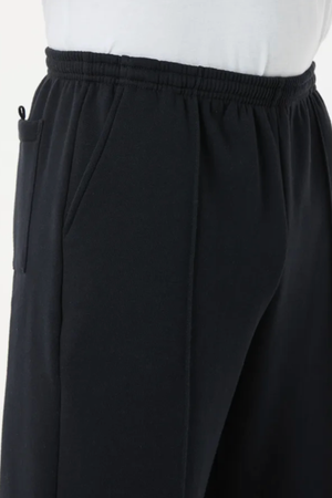 A close-up side view shows a person wearing Breakaway Classic Snowy Mt Fleece Pant in black, featuring an elastic waistband and pockets, paired with a white shirt—ideal for casual weekend wear.