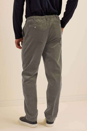 A person stands with their back to the camera against a light wall, wearing a navy long-sleeve shirt, dark slip-on shoes, and Breakaway Cordeaux Pant featuring an elasticised waist.
