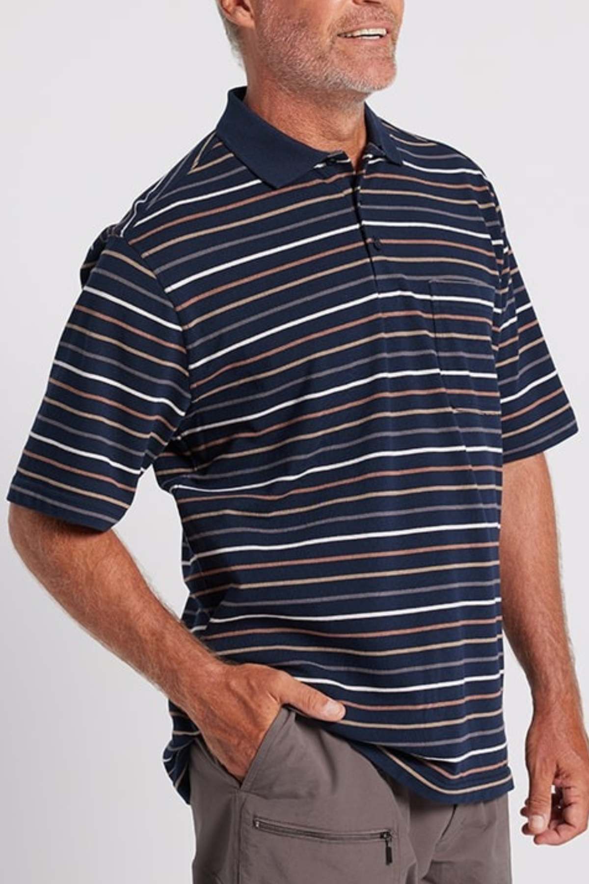 A person wearing a navy blue and white striped Breakaway Dariyan Cotton Pique Polo with short sleeves and a collar, paired with gray pants. The modern thin stripe design complements their beard as they stand against a plain background with one hand in their pant pocket.