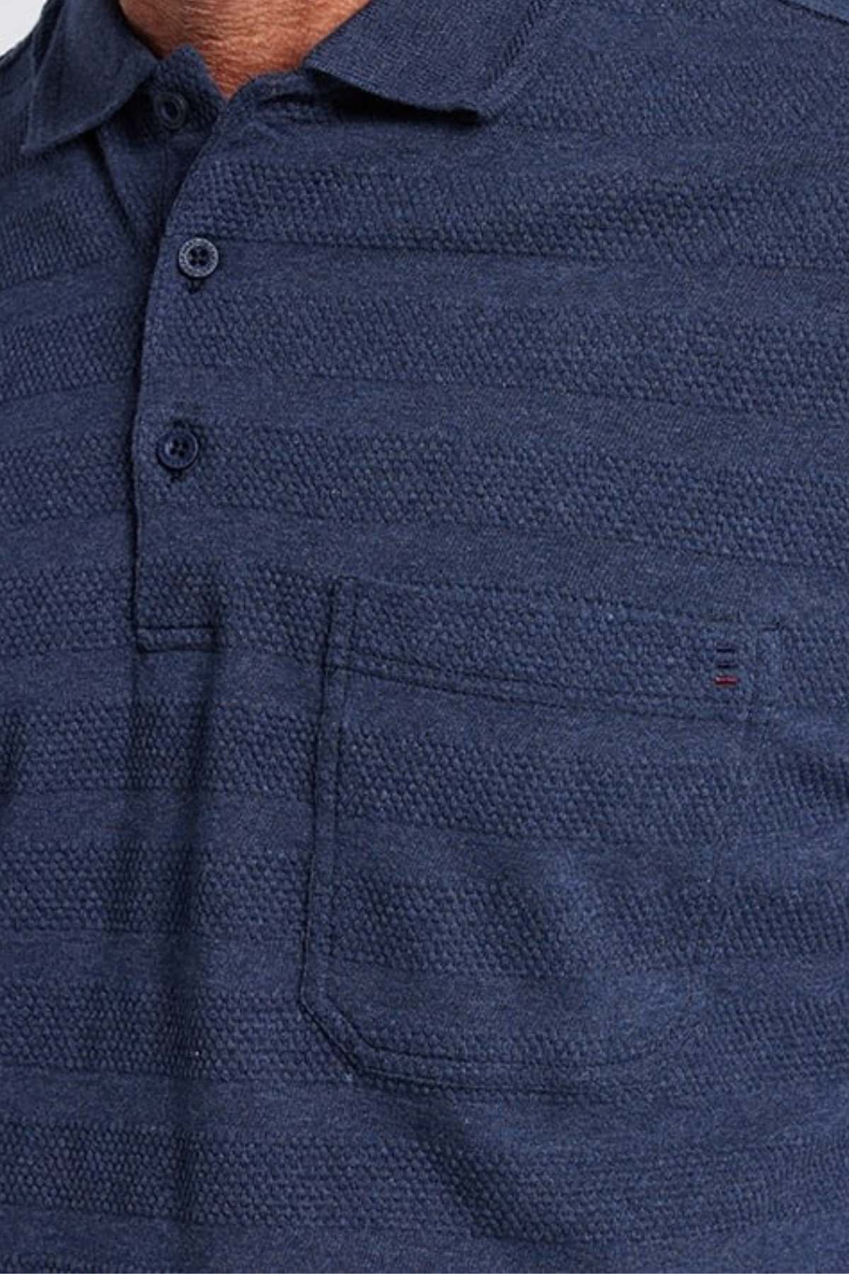 A close-up shot showcases a person donning the Breakaway Emil Polo in dark blue, distinguished by its elegant knit collar and chest pocket. Crafted from 100% cotton, this textured polo features a three-button placket and subtle horizontal stripes. The upper torso is prominently visible.