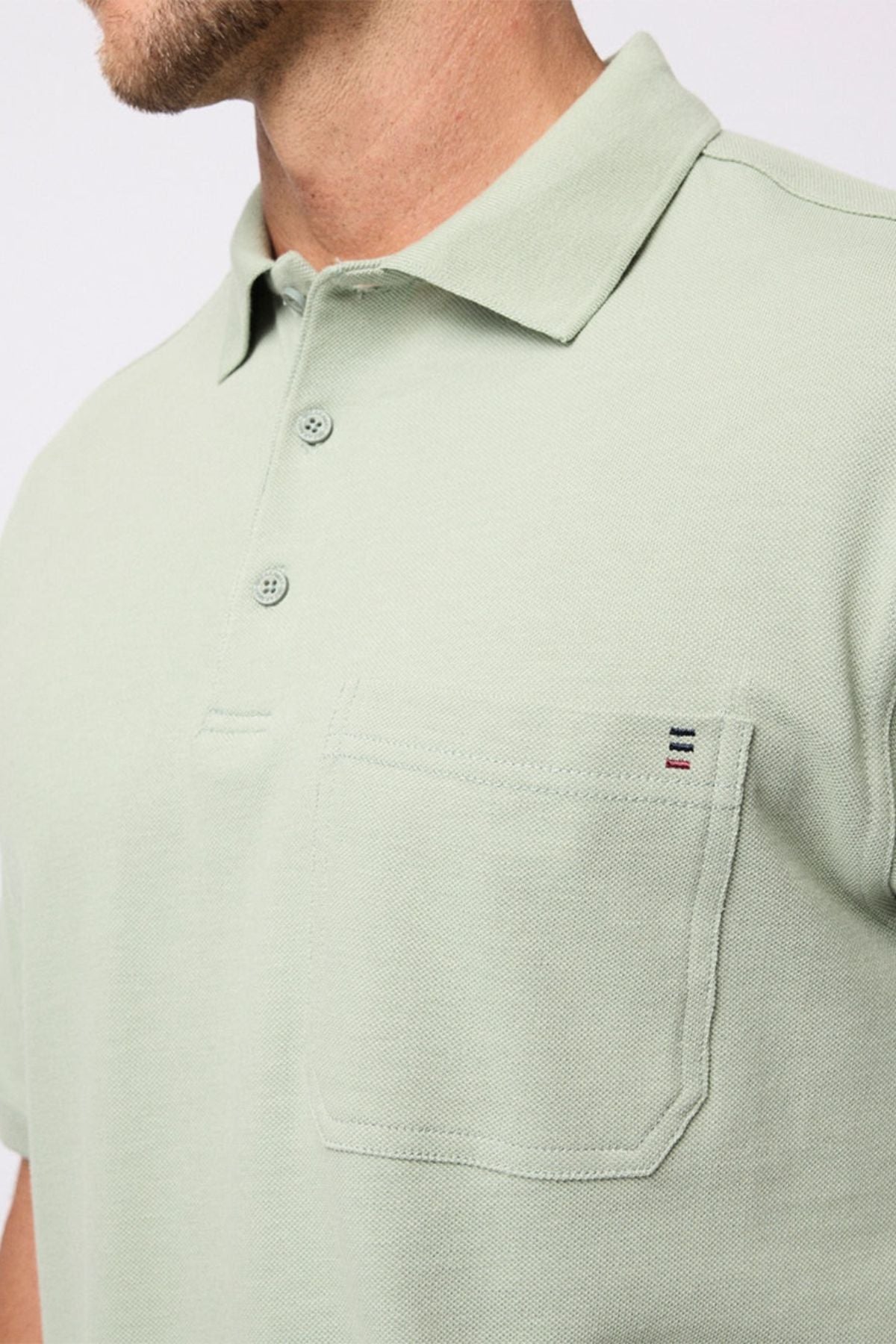 A close-up of a man wearing the Breakaway Fraser Cotton Pique Polo, a light green regular fit shirt with a collar, two buttons, and a chest pocket featuring a stitched detail of three horizontal colored lines.