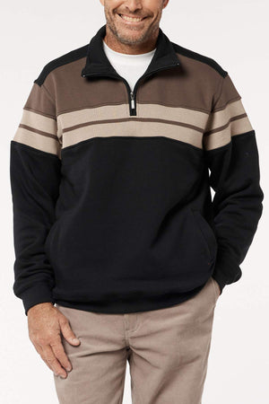 A man wears the Breakaway Henrich Snowy Mt Fleece Half Zip, featuring a wide brown and beige chest stripe, over a white T-shirt with light brown pants, standing with one hand in his pocket and smiling.