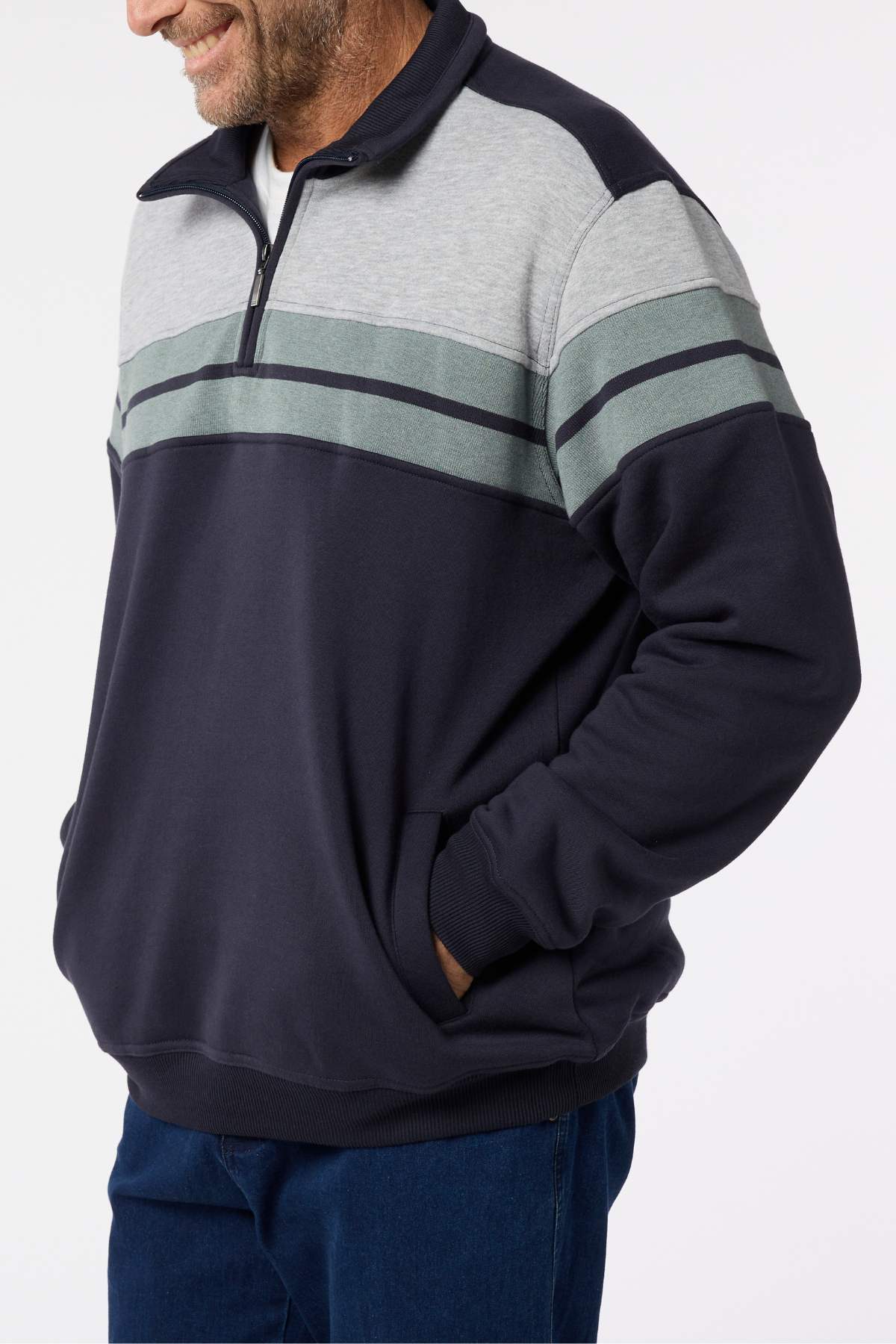 A man is shown from shoulders to hips, smiling with his hands in his pockets, wearing a Breakaway Henrich Snowy Mt Fleece Half Zip featuring navy blue and gray horizontal stripes.