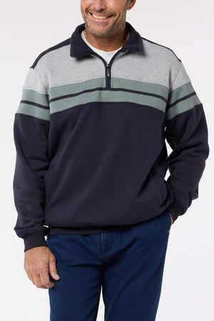 A man wears a Breakaway Henrich Snowy Mt Fleece Half Zip in navy blue and gray with green and gray chest stripes, paired with blue jeans. He stands smiling with one hand in his pocket.