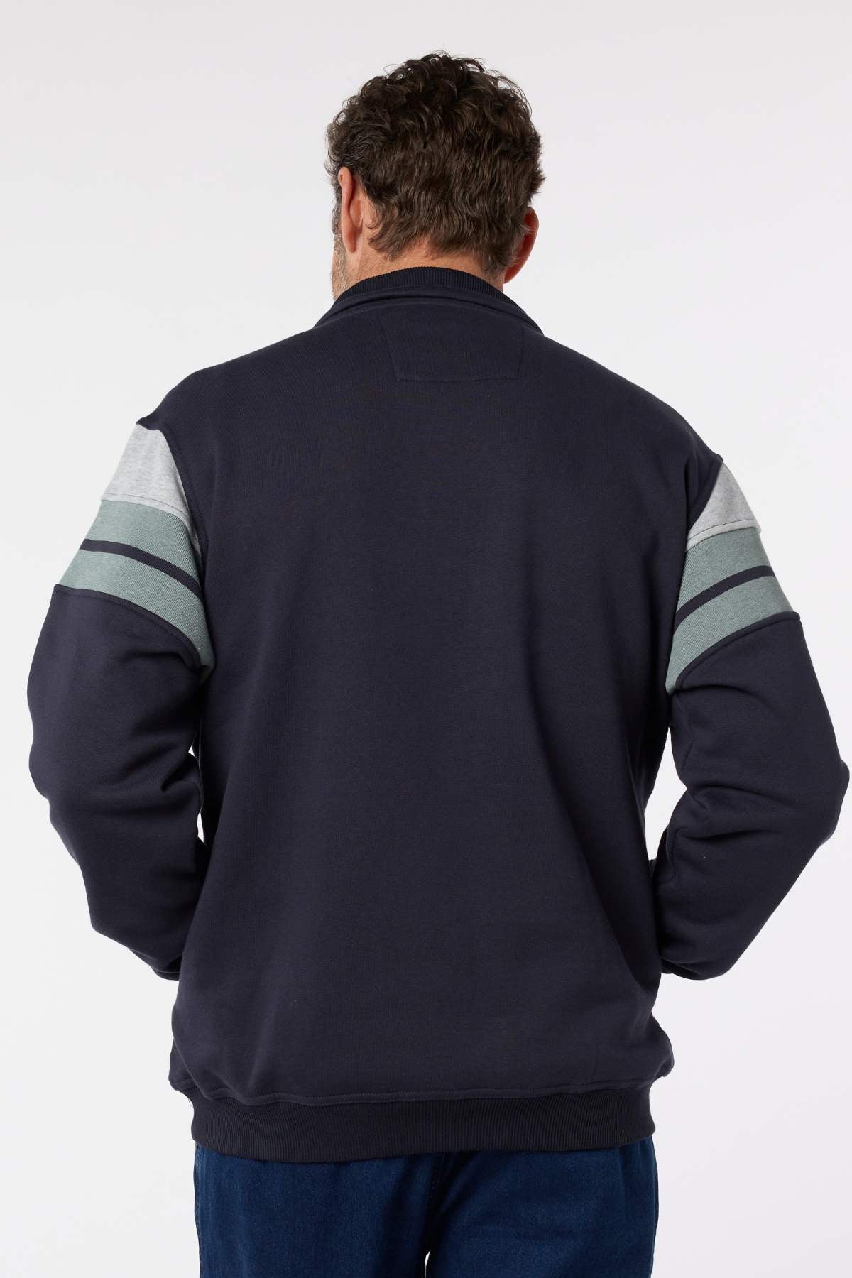 A man with short, curly brown hair is seen from behind wearing the Breakaway Henrich Snowy Mt Fleece Half Zip in dark navy, featuring light gray and green sleeve stripes. His arms hang relaxed by his sides against a plain white background.