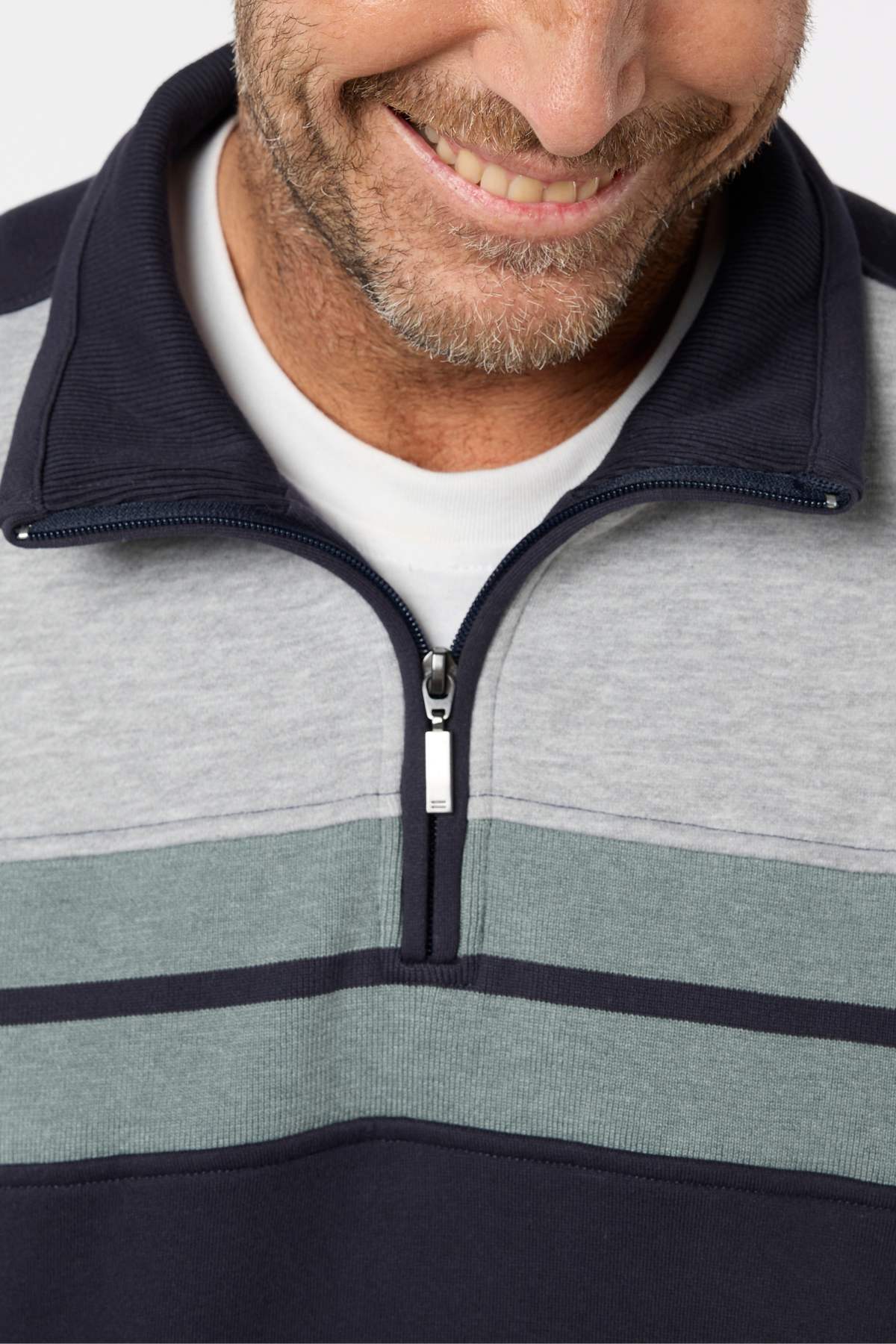 A smiling man with a short beard wears a striped Breakaway Henrich Snowy Mt Fleece Half Zip in gray and navy over a white T-shirt. Only his lower face and upper torso are visible in the photo.