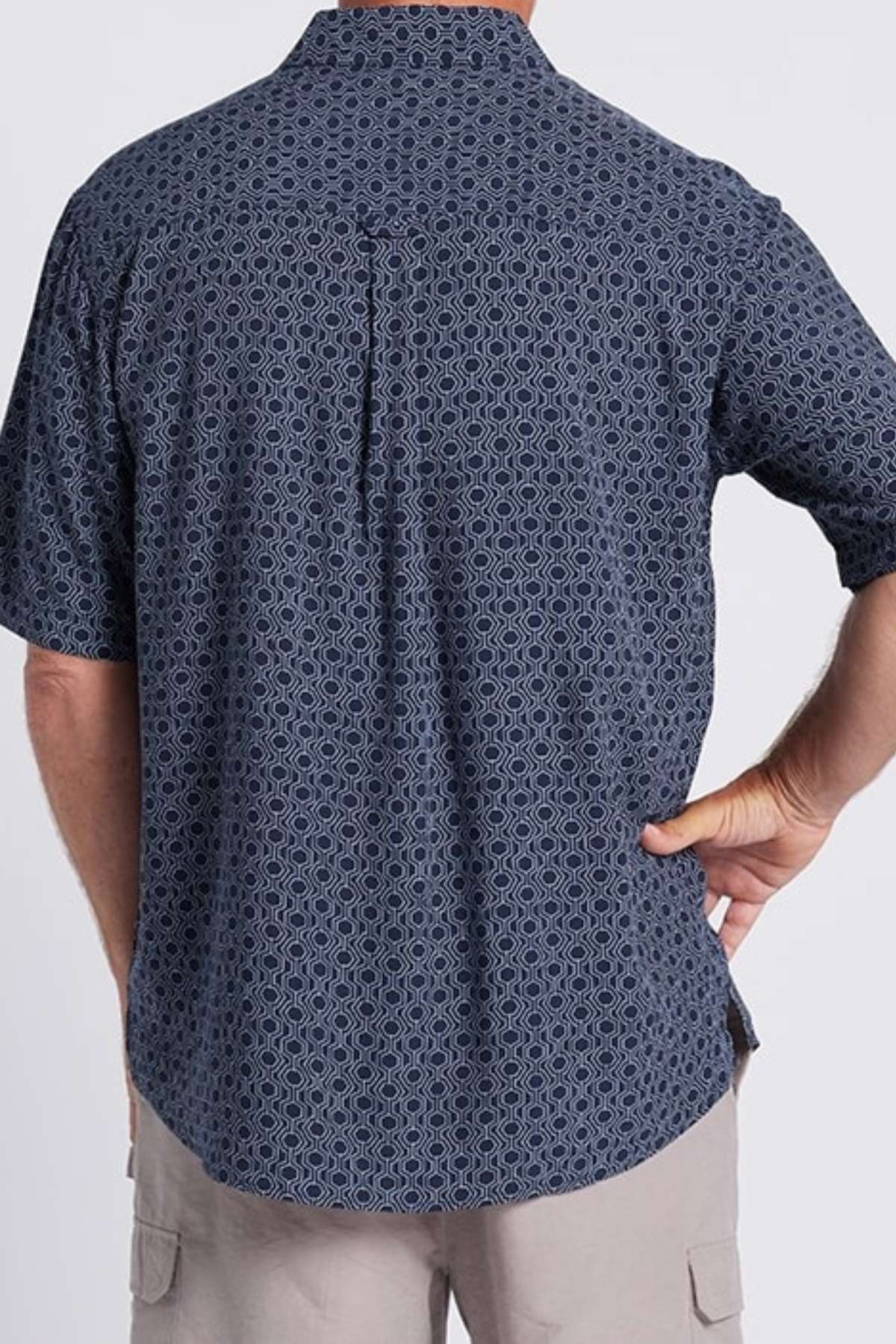 A person is standing with their back to the camera, wearing a Breakaway Jac Bamboo Shirt in dark blue with a geometric print. Their right hand rests on their hip, and they are also wearing beige shorts.