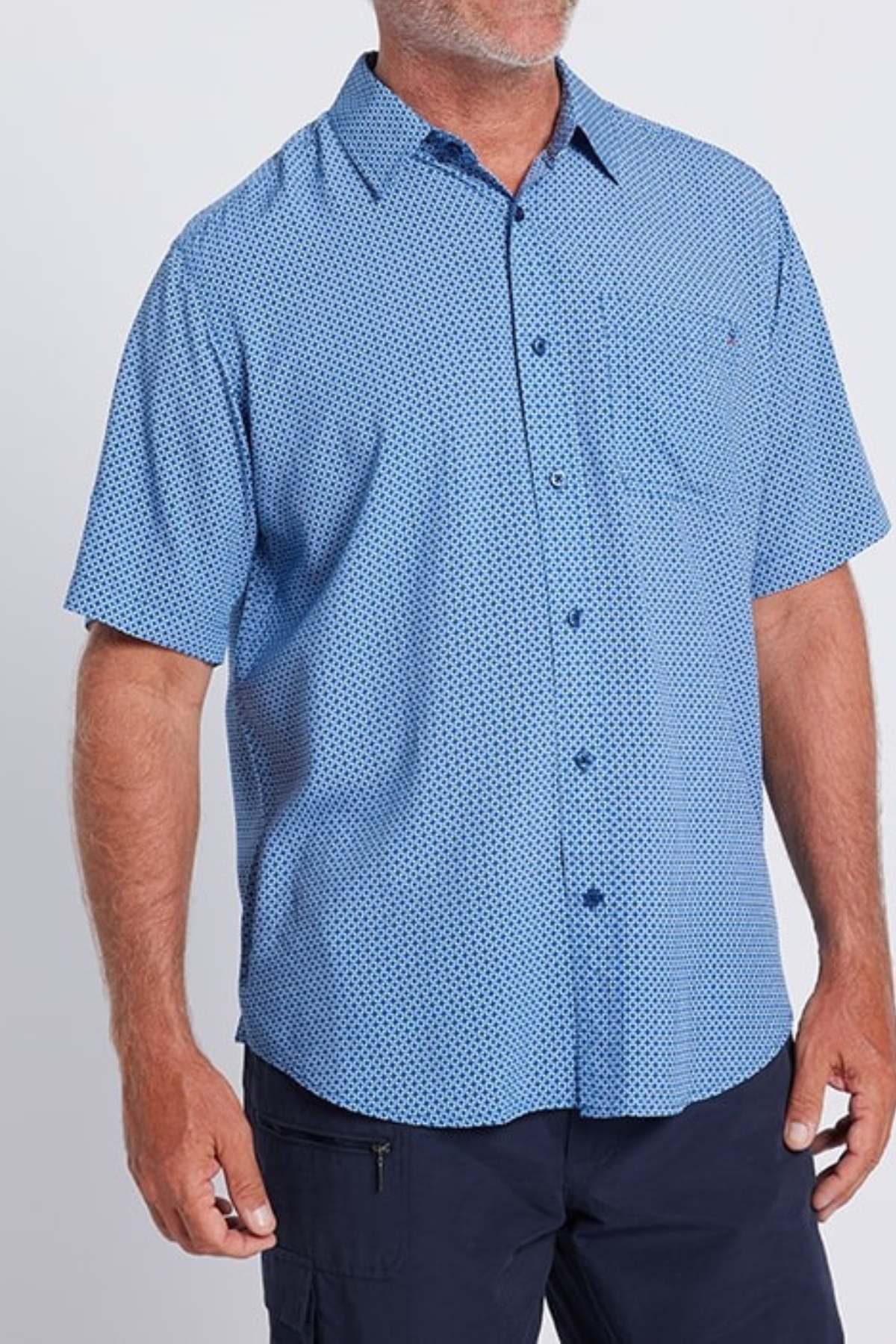 A man stands against a plain light background wearing the Breakaway Kre Bamboo Shirt—a short-sleeve, button-up limited edition shirt with a subtle geometric pattern—paired with dark pants.