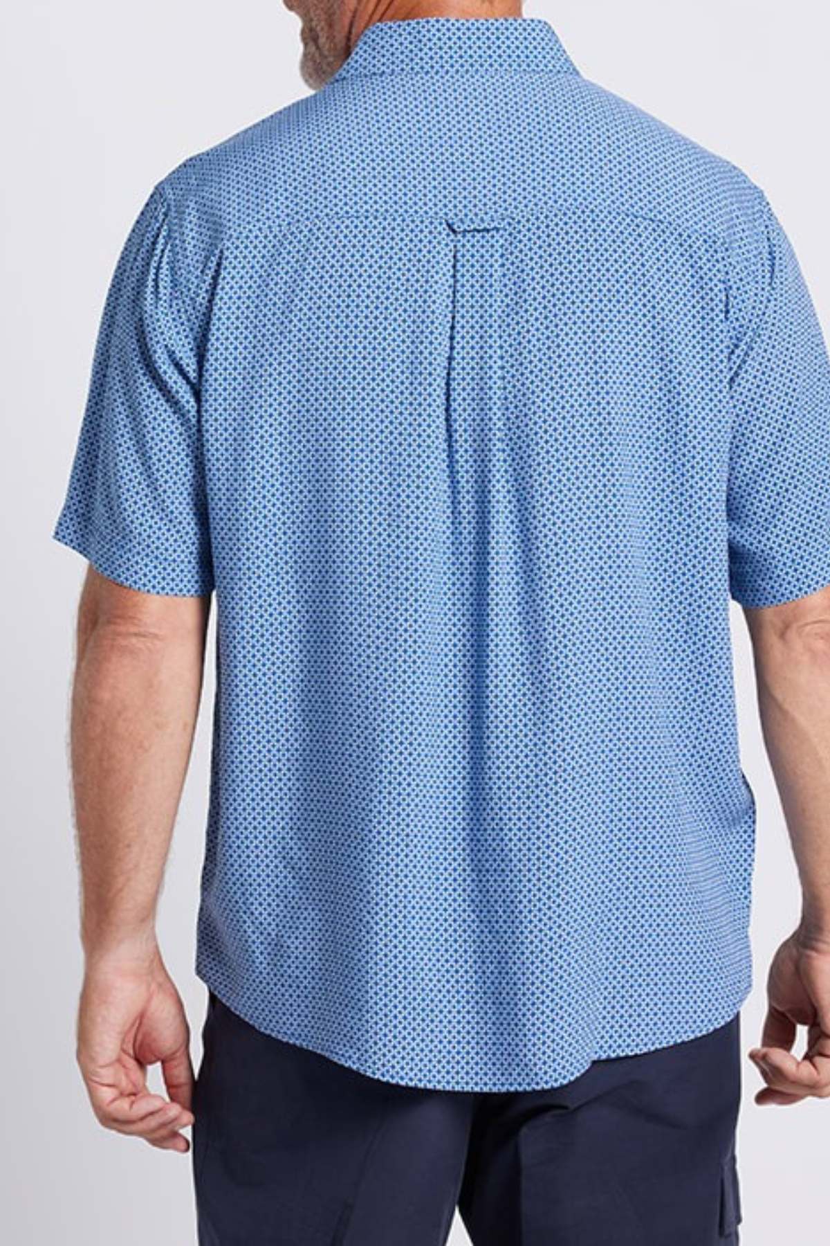 A man is shown from the back wearing a light blue Breakaway Kre Bamboo Shirt with a small geometric pattern and dark pants—an ideal choice for summer. The background is plain and light-colored.