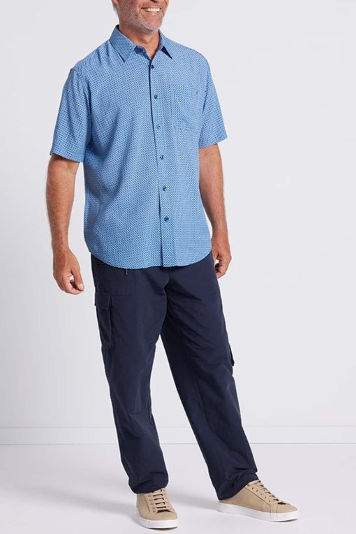 A man smiles in the Breakaway Kre Bamboo Shirt—a limited edition, light blue, short-sleeve button-up with a subtle pattern—styled with dark navy cargo pants and beige sneakers, all set against a plain white background. Perfect for your summer wardrobe!.