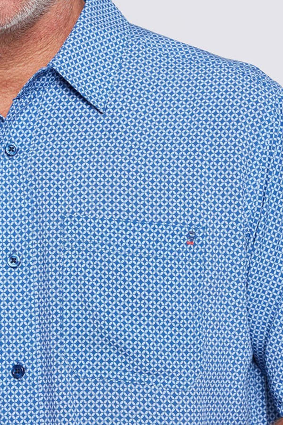 Close-up of a man in the Breakaway Kre Bamboo Shirt, featuring a blue geometric pattern, buttoned collar, and front pocket. Only part of his face and shoulder appear. This Limited Edition shirt is perfect for your summer wardrobe.