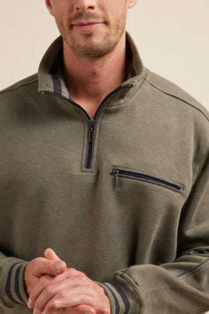 A person is wearing an olive green Breakaway Kyler Snowy Mt Fleece Half Zip, featuring a zippered chest pocket and black striped details on the collar and cuffs. The soft and warm fleece enhances the cozy winter vibe. The individual is clasping their hands together, visible from the shoulders to the mouth against a plain beige background.