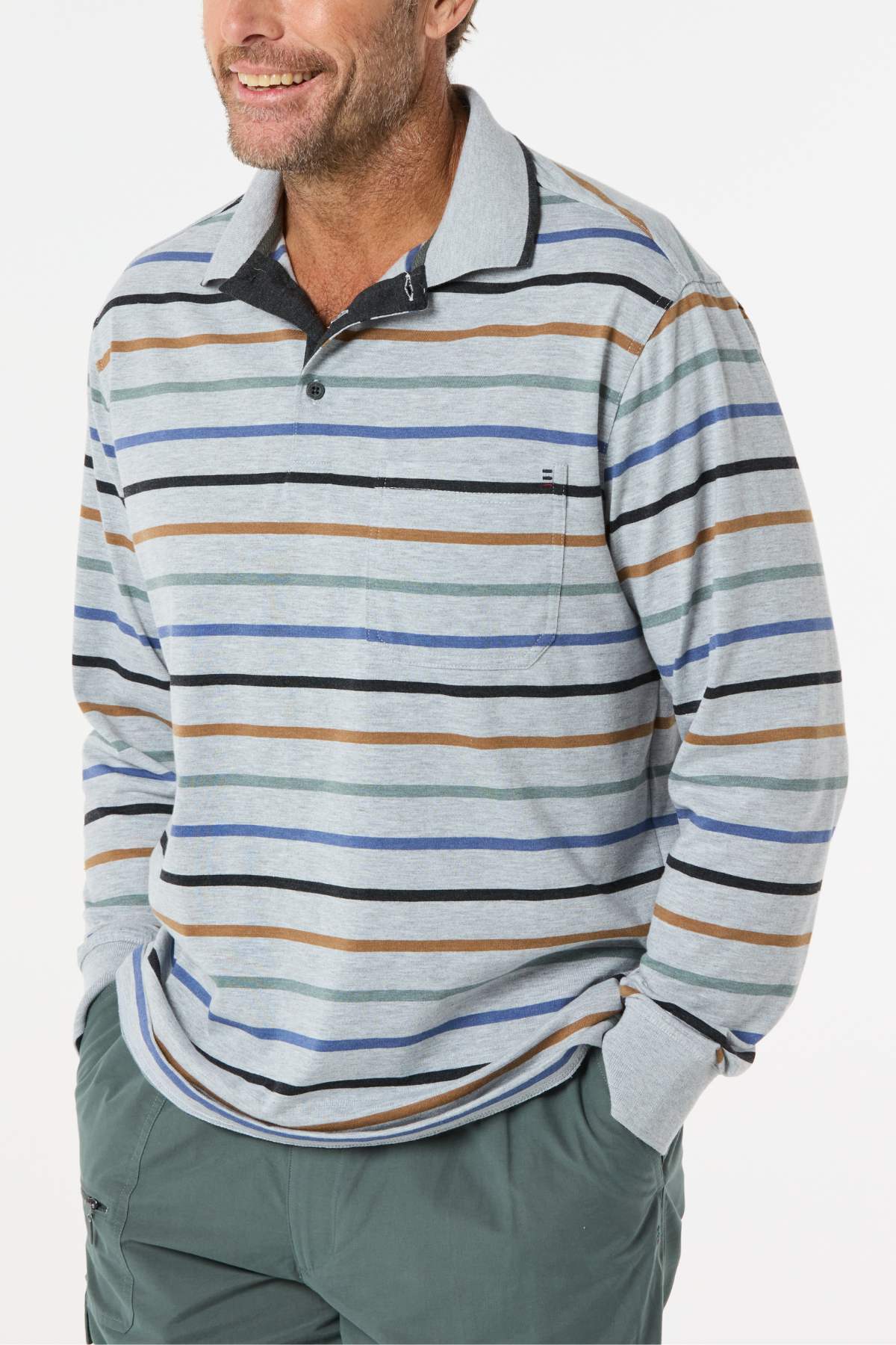 A man smiles with his hands in the pockets of his green pants, wearing a Breakaway Lendel Kinnersly Polo featuring horizontal blue, brown, and black stripes and rib knit cuffs.