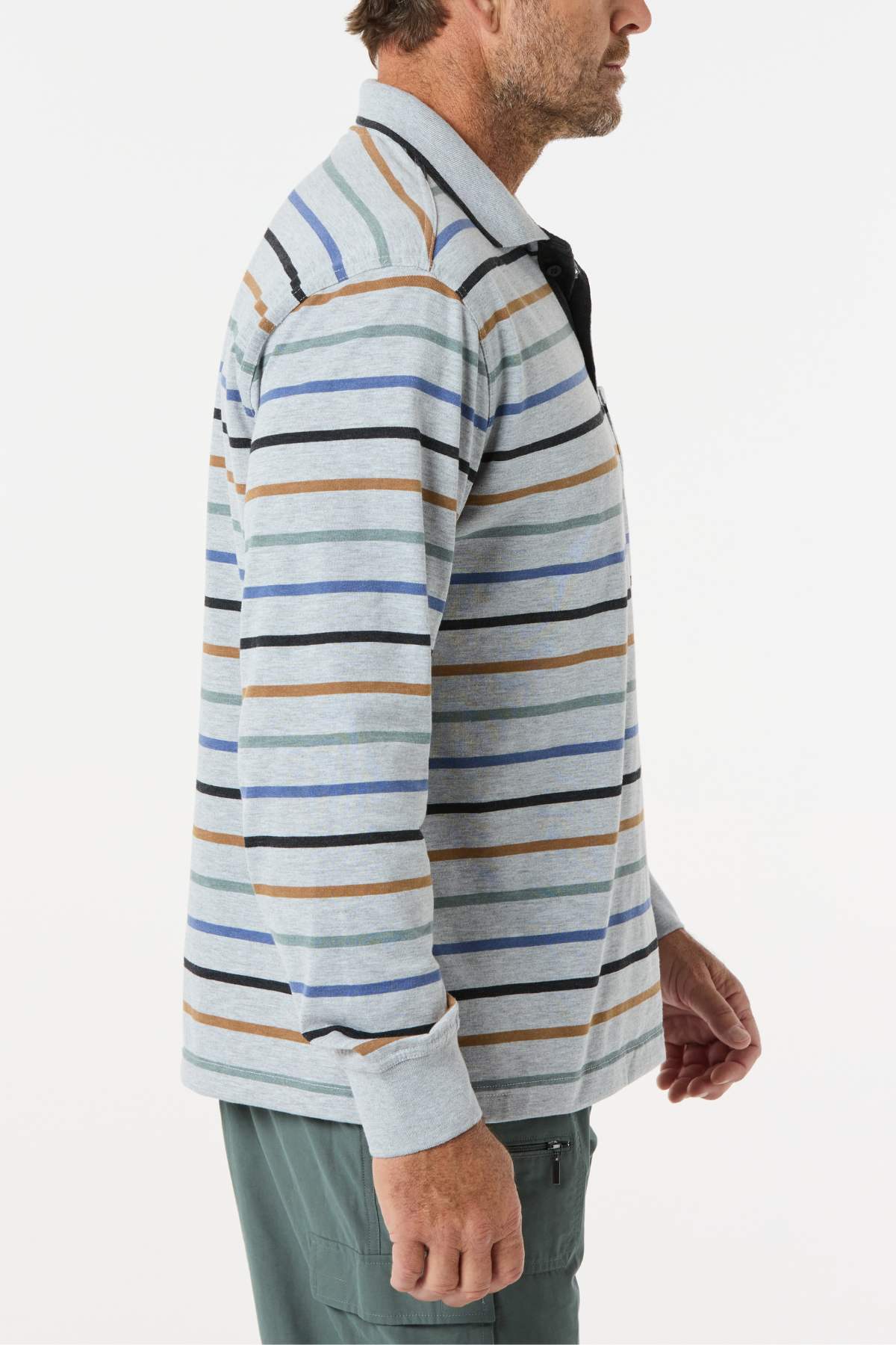 A man in profile, facing right, wears the Breakaway Lendel Kinnersly Polo—a light gray, long-sleeved shirt with blue, brown, navy, and black stripes and rib knit cuffs—paired with green pants.