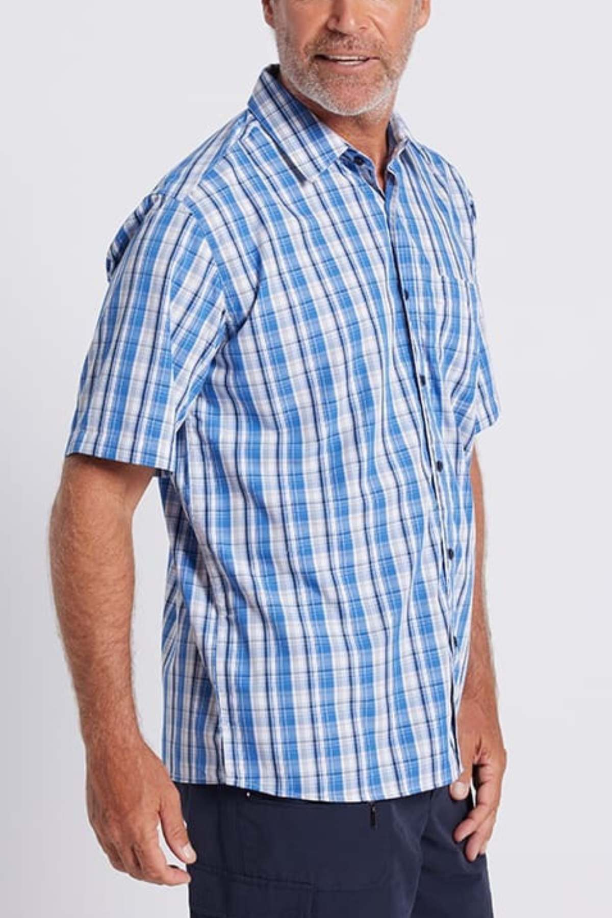 A person with a gray beard is wearing a serene seaside blue Breakaway Ora Bamboo Blend Shirt paired with dark pants. The background is a plain, light gray. With their left hand partially in their pants pocket, they radiate effortless elegance.