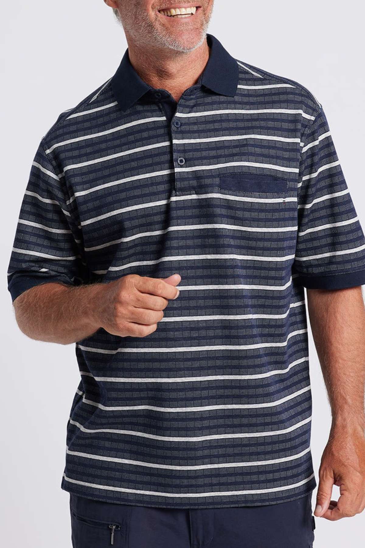 A man smiles while wearing the Breakaway Turner Micro Prima Polo, which displays a blue and white striped pattern. His shirt has a navy collar and features a single chest pocket. He's standing against a plain light gray background, showcasing his short, graying hair. Only his upper torso and part of his arms are visible.