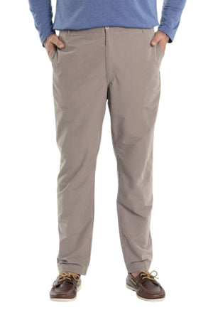 A person wears Breakaway Woodbury Pull On Pants in light brown with an elastic waist, a blue long-sleeve shirt, and brown boat shoes, standing hands-in-pockets against a white background.