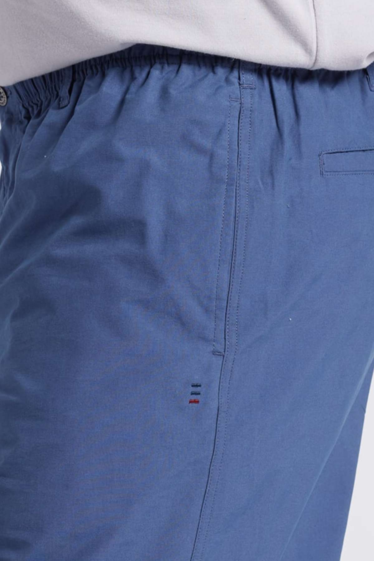 Close-up of a person wearing the blue Breakaway Woodbury Short, featuring an adjustable elastic waistband and a small stitched design near the pocket. The design showcases three parallel lines in red, white, and navy blue. The person is also wearing a light-colored top.