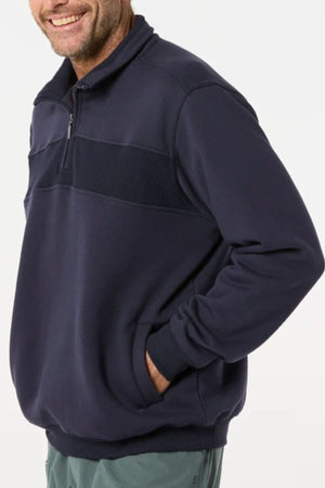 A man wears the Breakaway Zed Snowy Mt Fleece Half Zip in navy, featuring a zip collar, ribbed chest panel, and cozy fleece lining—an essential layering piece for any wardrobe as he smiles with one hand in his pocket.