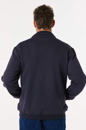 A man with curly hair stands with his back to the camera, wearing a Breakaway Zed Snowy Mt Fleece Jacket in navy blue and blue pants, set against a plain light background.