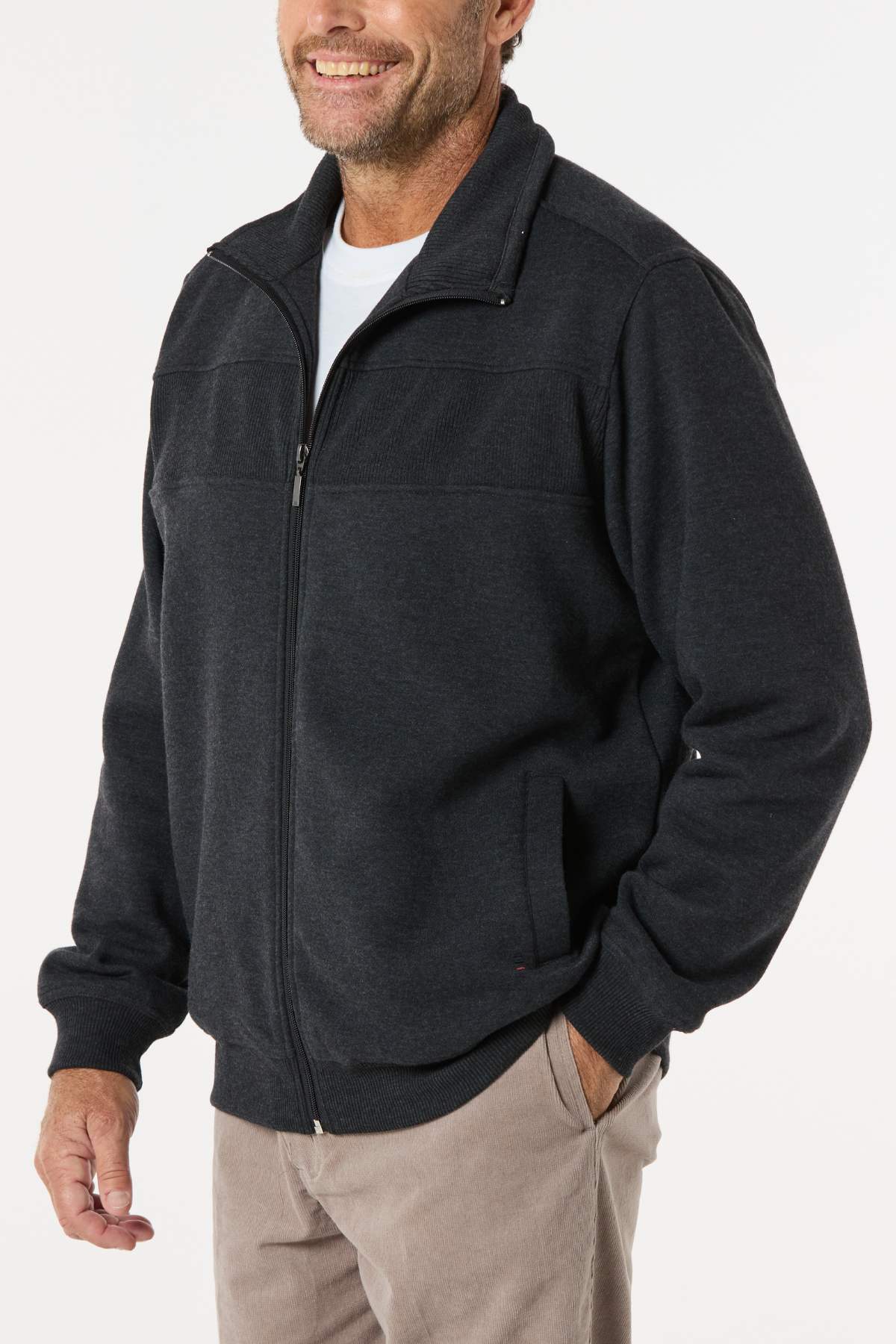 A smiling man wears the Breakaway Zed Snowy Mt Fleece Jacket over a white shirt and tan pants, standing with one hand in his pocket against a plain light background.