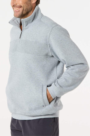 A man smiles with his left hand in his pocket, wearing the Breakaway Zed Snowy Mt Fleece Half Zip in light gray with ribbed chest detailing. The background is plain white.