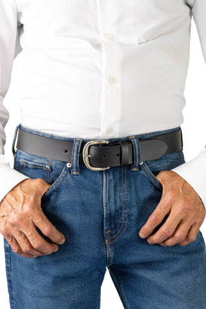 A person stands with hands on hips, wearing a white button-down shirt tucked into blue jeans, accessorized with the Buckle 5092 Buffalo Top Grain Belt.