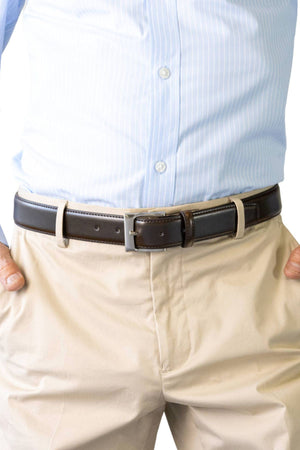 A person wearing a light blue striped dress shirt tucked into beige pants with the Buckle 5115 Rogue Deluxe Leather Belt, hands resting in pockets.
