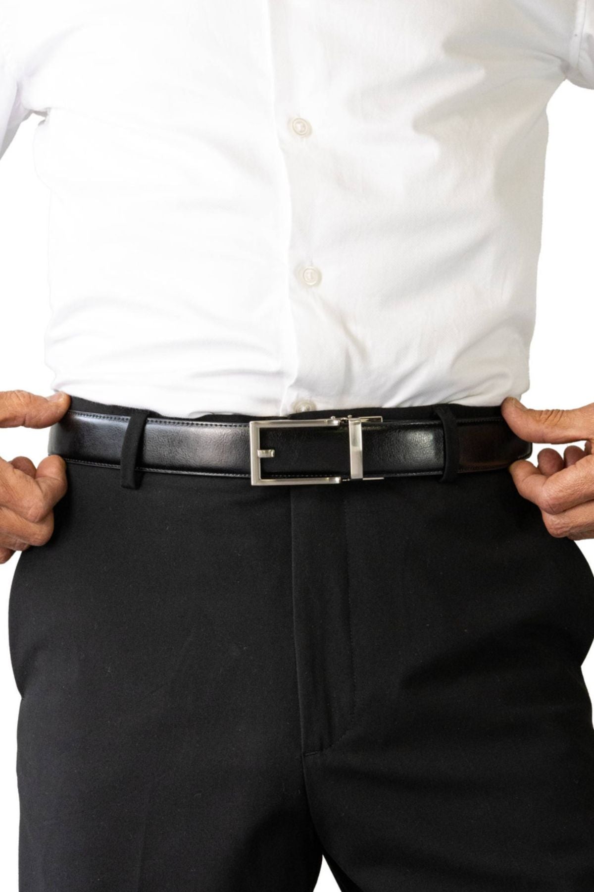 A person in a white button-up shirt and black pants adjusts the Buckle 5129 Hamilton Auto Club Belt, an adjustable genuine leather belt with a silver buckle. Only their torso and hands are visible against a white background.