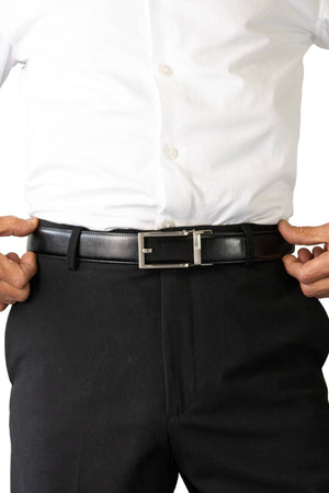 A person in a white button-up shirt and black pants adjusts the Buckle 5129 Hamilton Auto Club Belt, an adjustable genuine leather belt with a silver buckle. Only their torso and hands are visible against a white background.
