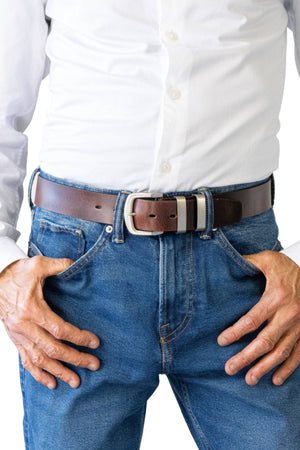 A person stands with hands on hips, wearing a white button-down shirt, blue jeans, and the Buckle 5538 Natural Full Grain Belt featuring an antique nickel buckle.