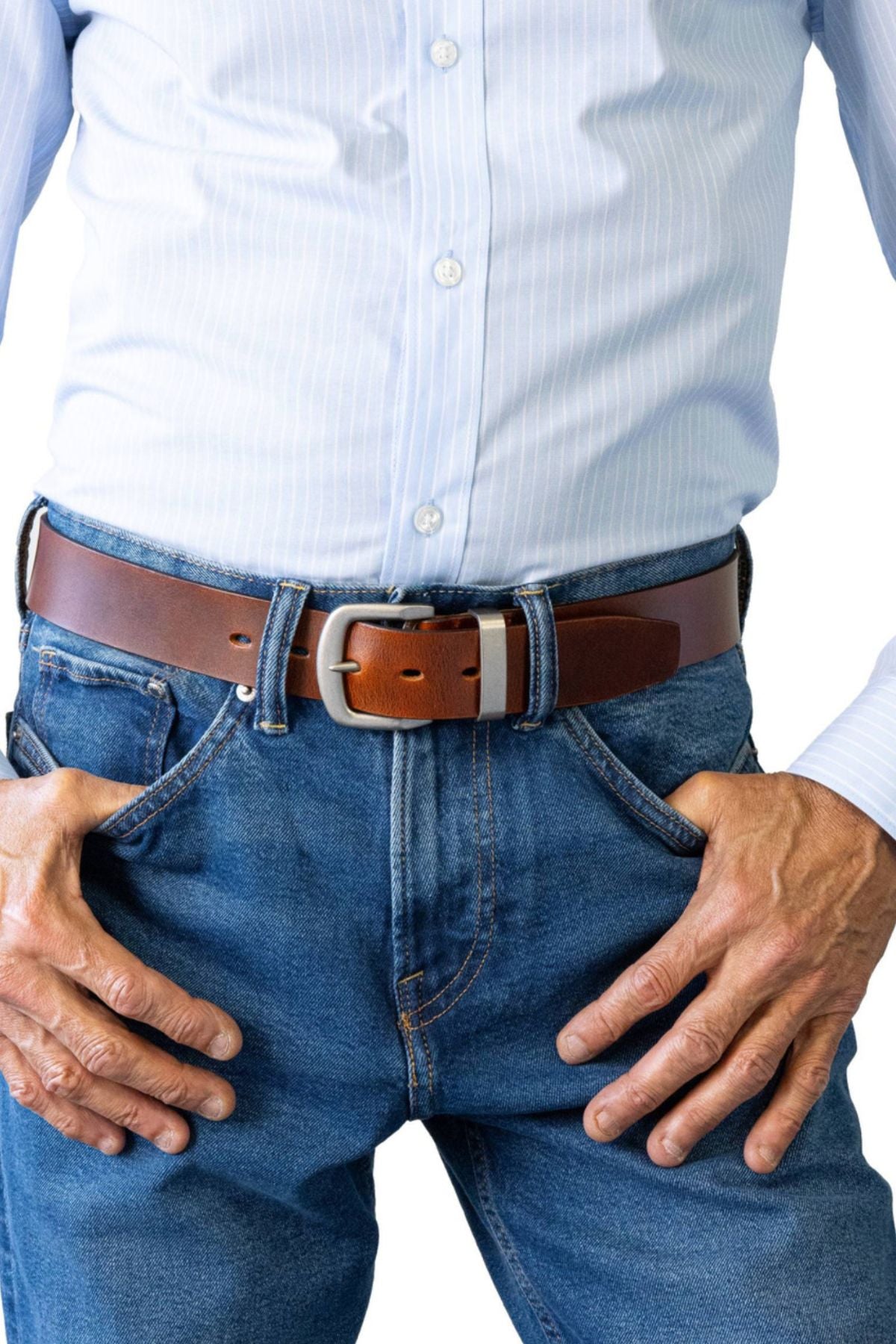 A person wearing a light blue striped button-up shirt tucked into blue jeans, accessorized with the Buckle 5538 Natural Full Grain Belt, rests their hands on their hips.