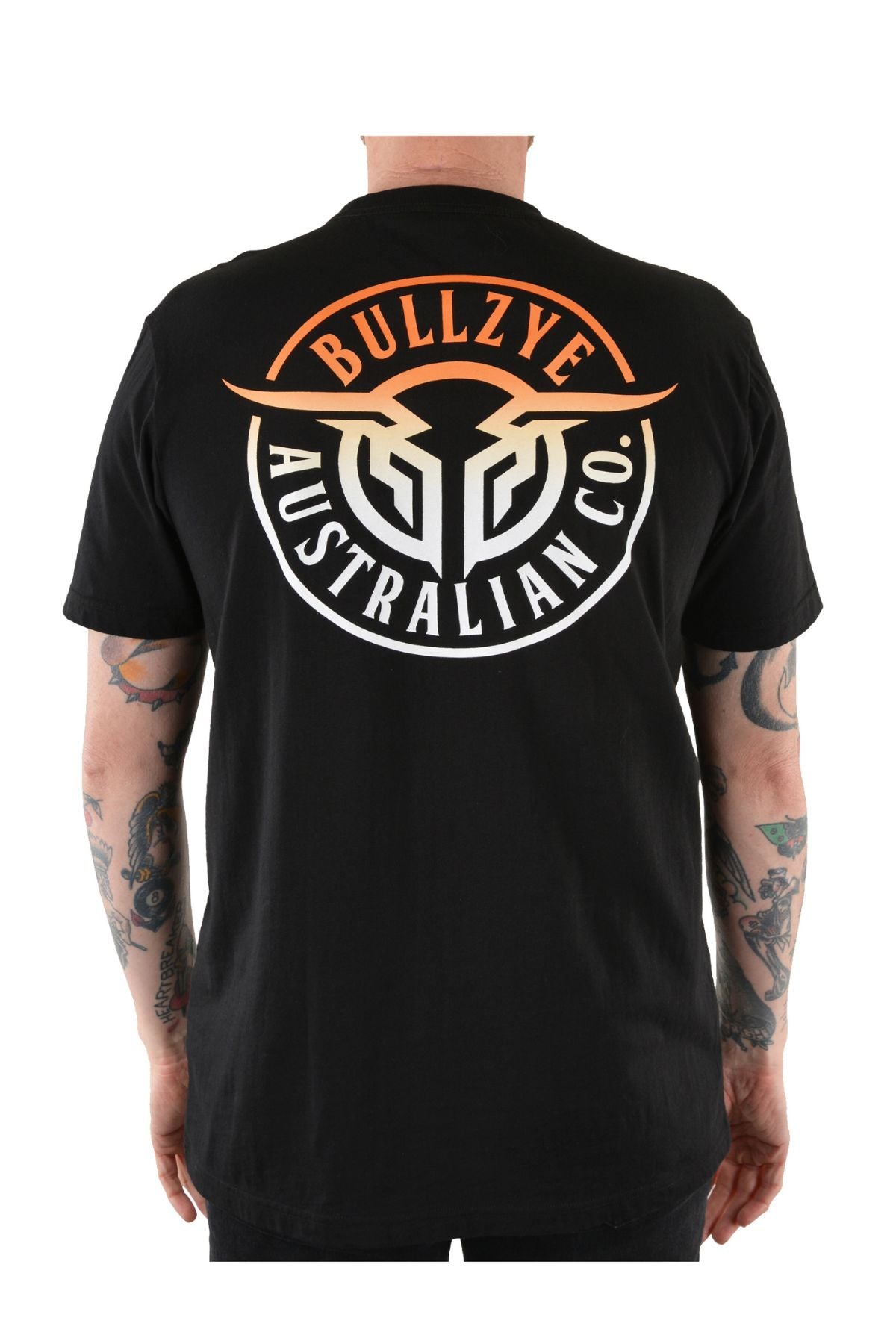 A tattooed person wears the Bullzye Bullring Tee, a black cotton jersey featuring a bold "BULLZYE AUSTRALIAN CO." back print in white and orange. The rear-view photo showcases the tee’s standout design.