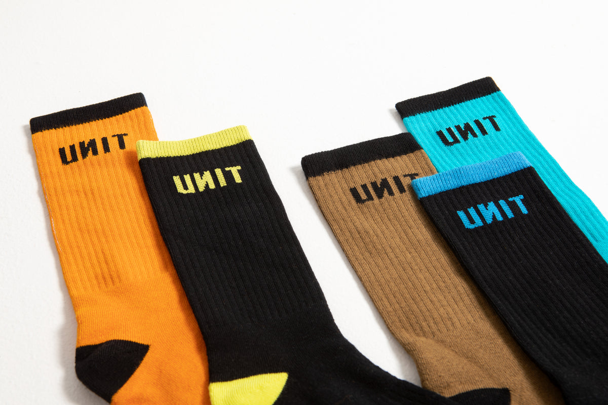 The UNIT React Bamboo 5 Pack Socks, shown on a white surface, feature bold UNIT logos and unique orange, black, brown, and turquoise color combos. Each pair offers anti-bacterial protection for added comfort.