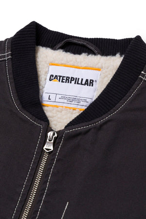 Close-up of a black CAT Canvas Utility Sherpa Lined Vest, featuring a partially open zipper, white sherpa lining, visible stitching, and a label with the CAT brand name, size L, and care instructions.