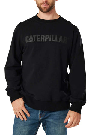 A man with light skin and a short beard is standing against a white background, wearing a black CAT Crewneck Sweatshirt. The sweatshirt prominently features "CATERPILLAR" printed in dark grey across the chest, and is crafted from durable fabric with a soft fleece lining. He pairs it with blue jeans.