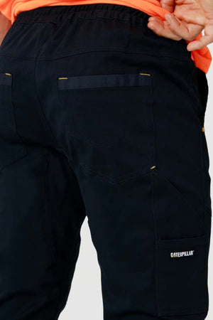 Close-up of a person wearing black CAT Dynamic Slim Fit Pant with visible back pockets and a "Caterpillar" logo on the side pocket; part of an orange shirt is also visible.