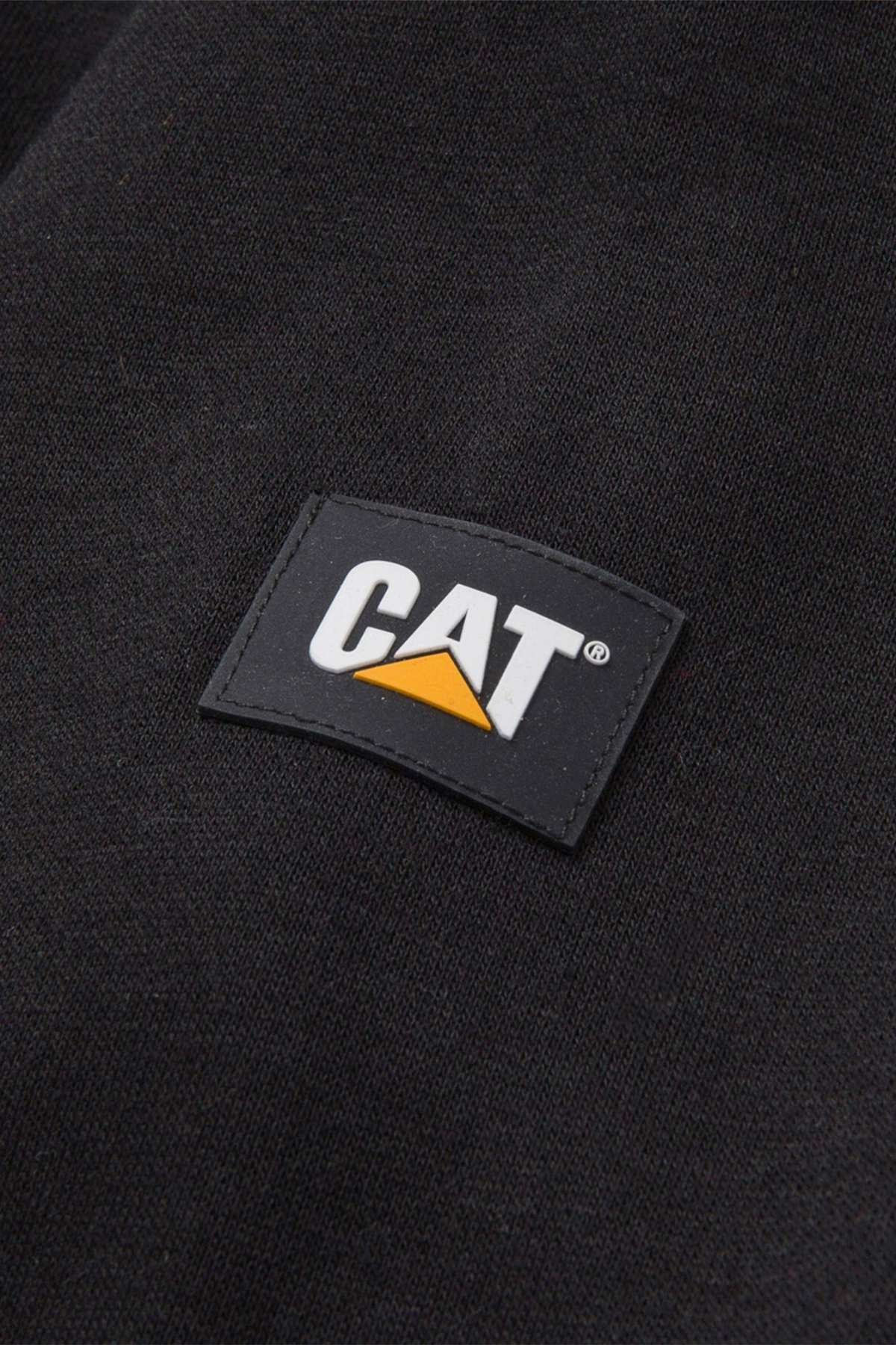 Close-up of the fabric shows a small rectangular logo patch. The patch is black with "CAT" in white capital letters and a yellow triangle beneath the "A". The dark-colored fabric, which appears to be black, suggests it could be part of the CAT Essential Hooded Sweatshirt by Caterpillar Inc.