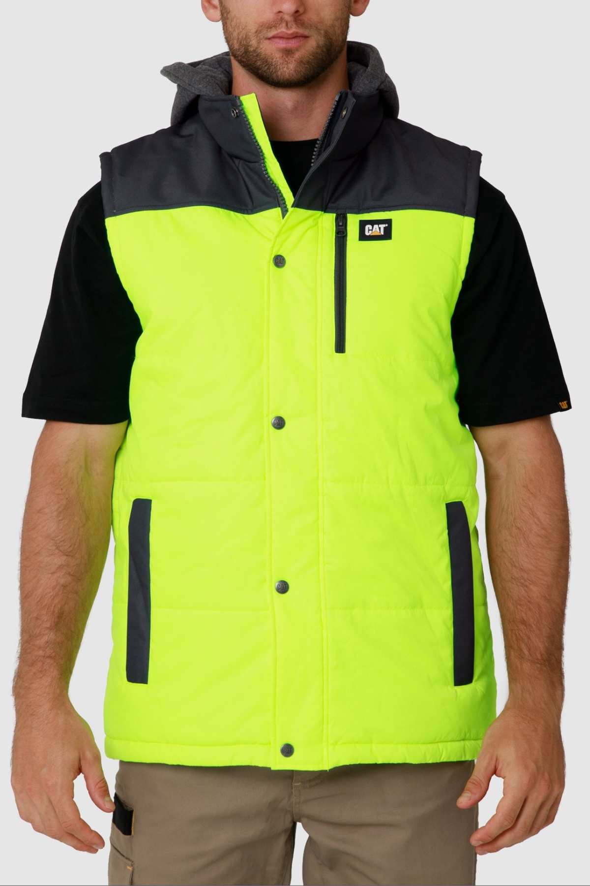 A person wears the CAT Hi Vis Hooded Work Vest, featuring a bright yellow color with black shoulders over a black short-sleeve shirt. The water-resistant vest includes multiple pockets and displays a small chest logo, all set against a plain white background.