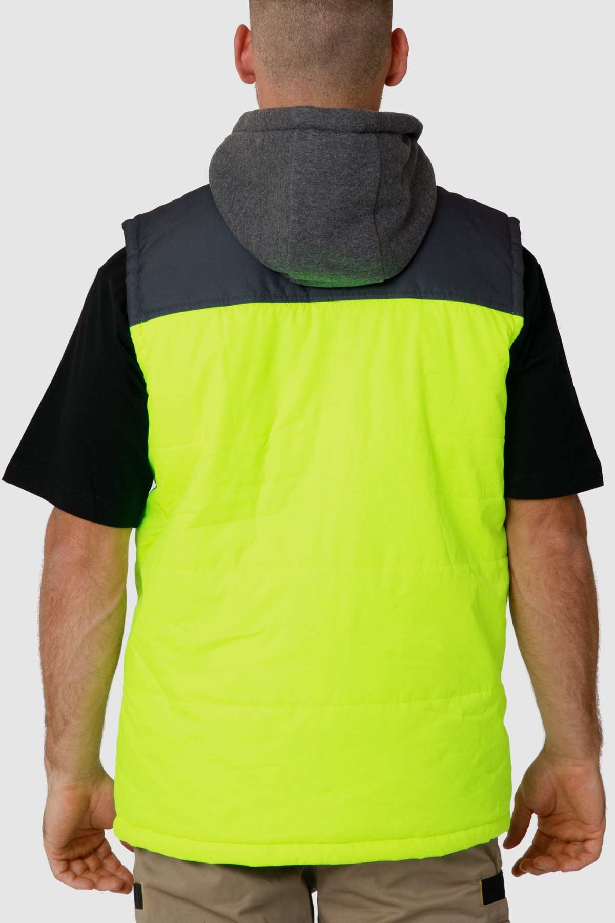 A person with short hair faces away from the camera, showcasing a CAT Hi Vis Hooded Work Vest over a black t-shirt. The neon yellow stands out against the plain white background, and the gray hood adds a sleek touch.