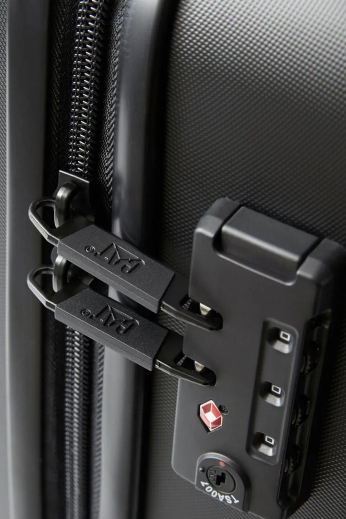 Close-up of the CAT Industrial Plate 28" Trolley, a black hard-shell expandable suitcase. Features include two zipper pulls secured in a TSA-approved combination lock, with visible textured surface and zipper detail.