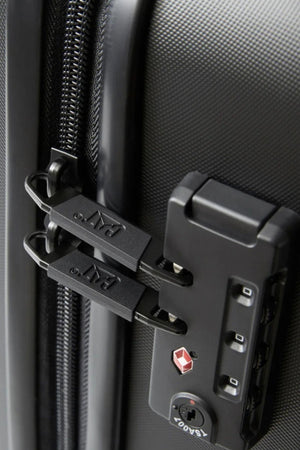 Close-up of the CAT Industrial Plate 28" Trolley, a black hard-shell expandable suitcase. Features include two zipper pulls secured in a TSA-approved combination lock, with visible textured surface and zipper detail.