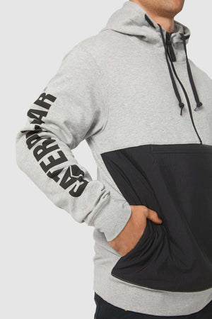 A person in a gray and black CAT Stillwater 1/4 Zip Hoodie with "CATERPILLAR" on the sleeve stands casually with a hand in the front pocket. The hoodie includes a drawstring hood and S3 Cord Management for convenience.