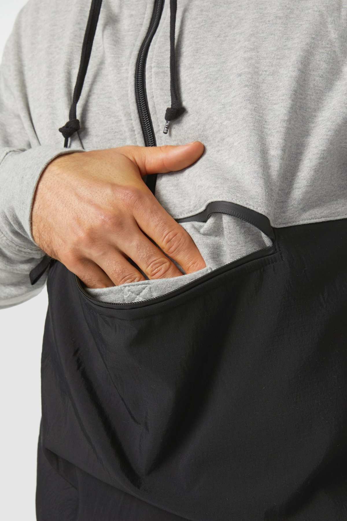 A person wearing a CAT Stillwater 1/4 Zip Hoodie in gray and black is placing their hand into the front pocket. The hoodie features a zipper and drawstrings for convenience, and its stylish design stands out against the plain white background.