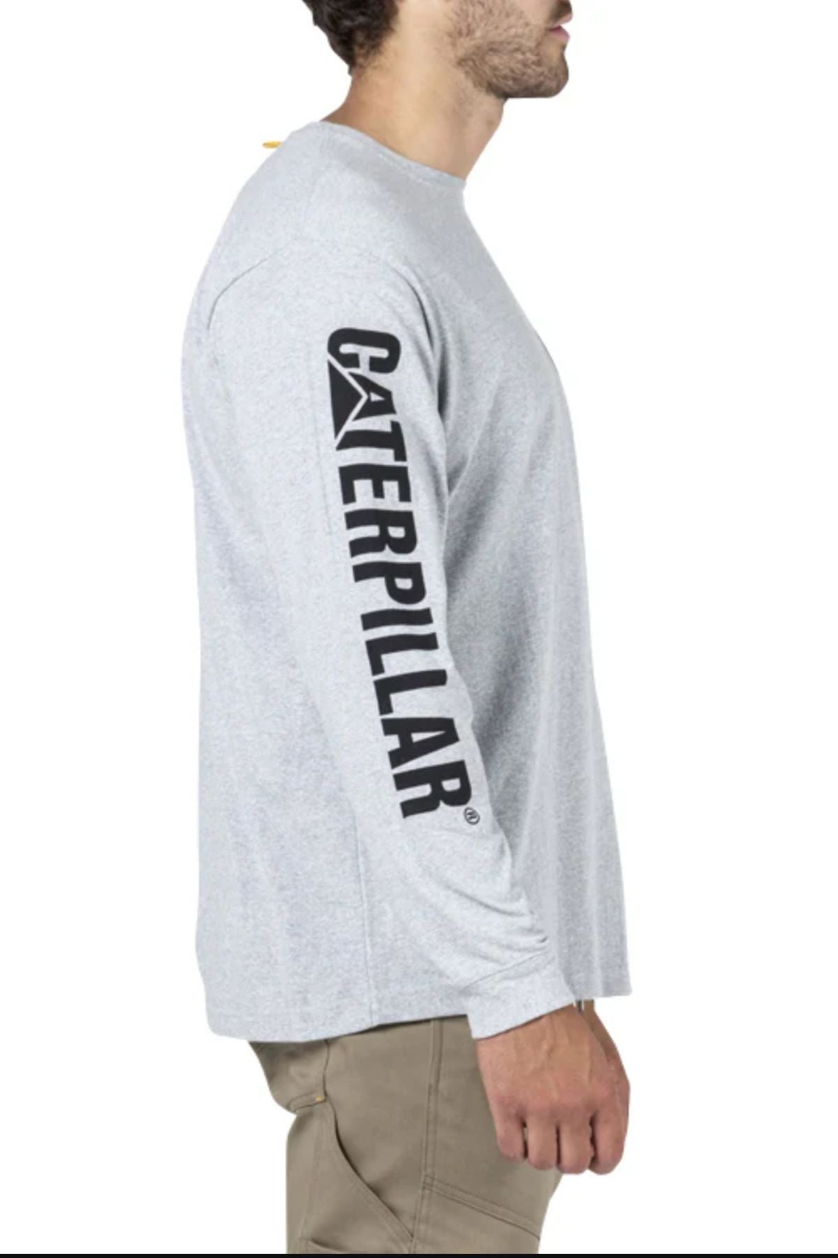 A man in a gray CAT Trademark Banner Long Sleeve Tee and khaki pants stands in profile. The comfortable cotton shirt features “Caterpillar” printed boldly down the sleeve.