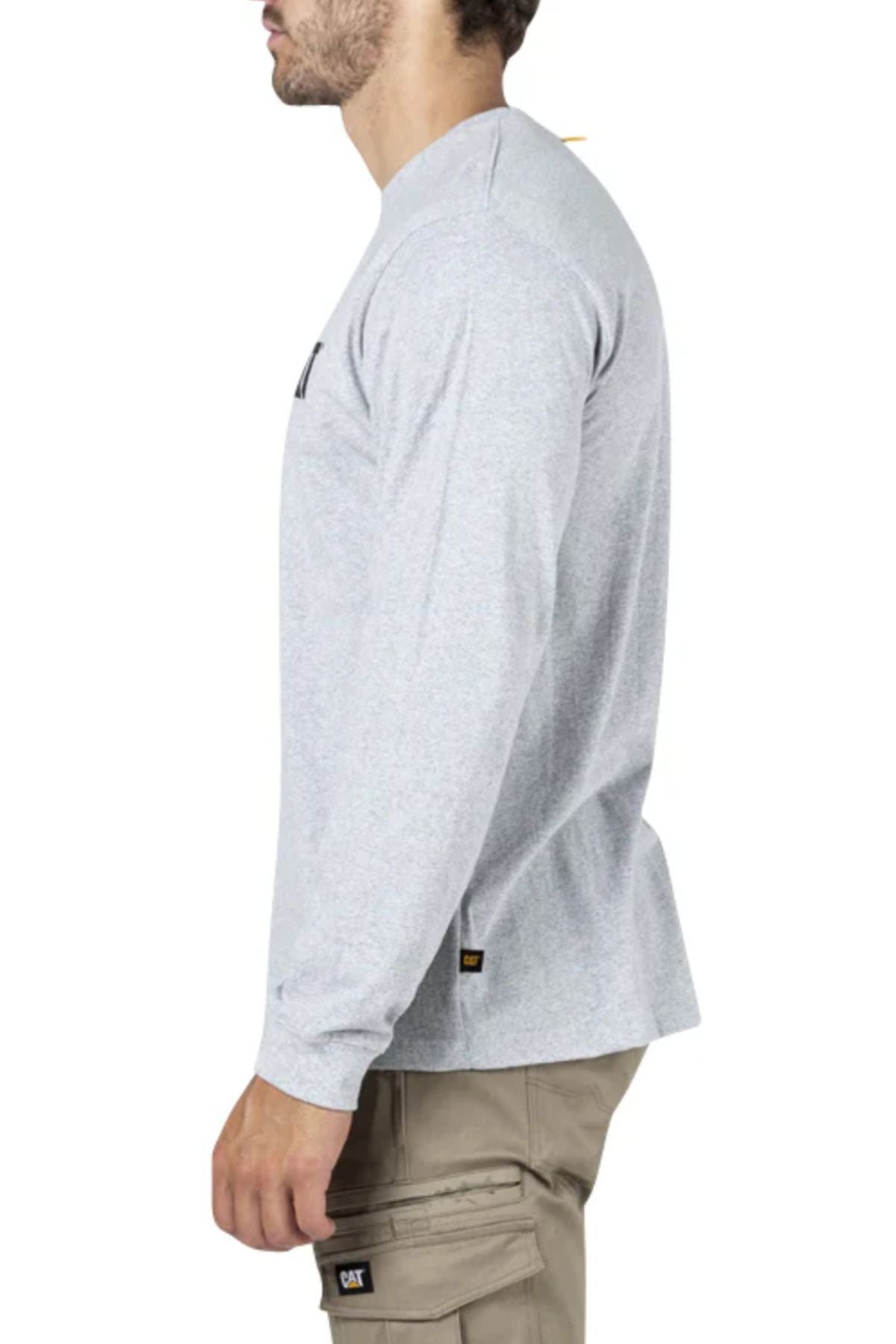 A man in profile wears a light gray CAT Trademark Banner Long Sleeve Tee and beige cargo pants with a black CAT logo tag on the pocket, styled in neutral tones against a plain white background.