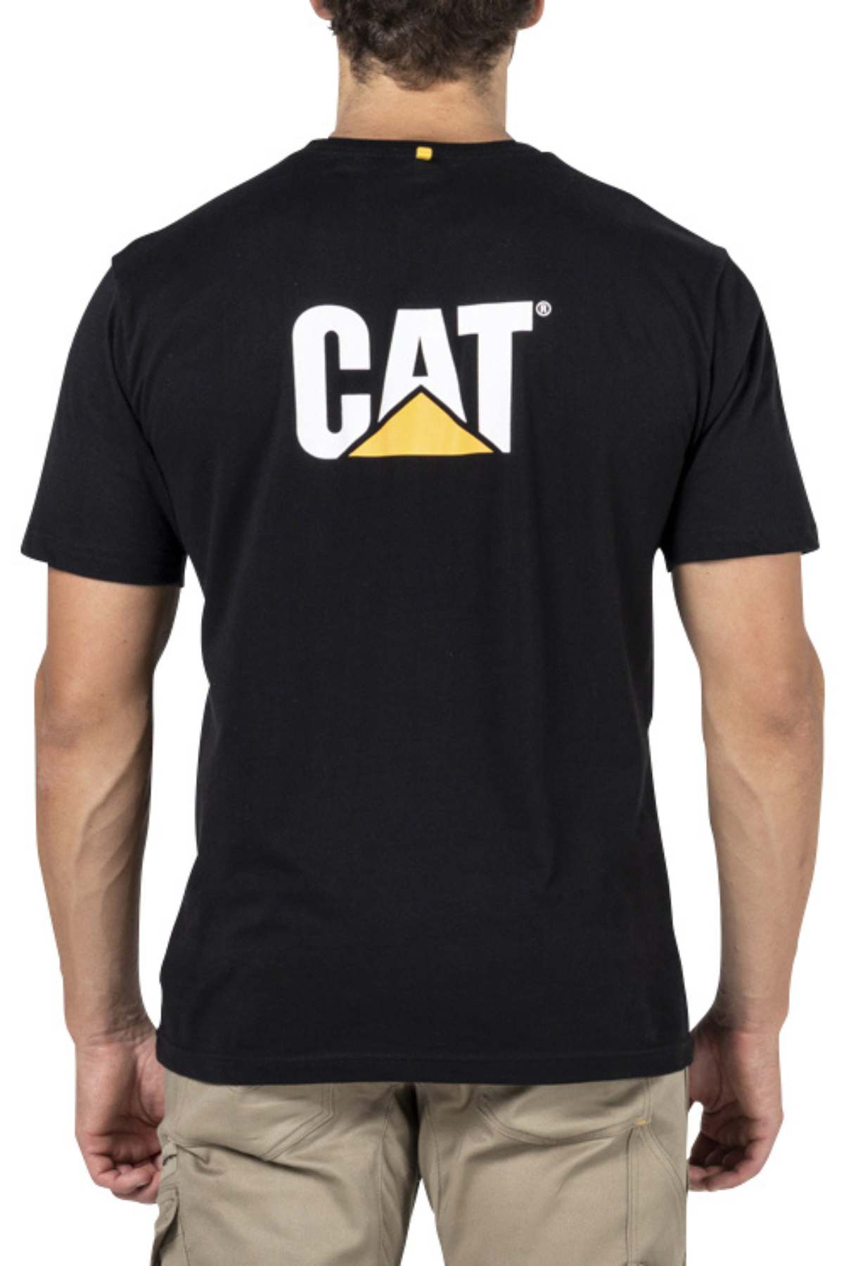 A person stands with their back to the camera, wearing a black CAT Trademark Tee featuring the CAT logo in white, yellow, and black on the back, paired with light-colored cargo pants.