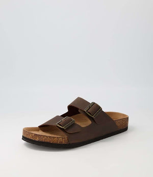 The Colorado Karra Crazyhorse Slide is a single brown leather sandal featuring two adjustable buckle straps, a contoured cork footbed for comfort, and a slip-resistant black sole, shown on a plain light gray background.