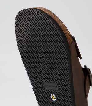 Close-up of the Colorado Karra Crazyhorse Slide's brown leather sole, showcasing a detailed zigzag tread, brand markings, cork footbed, and buckle strap—ideal for anyone seeking comfortable, stylish footwear.